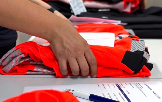 Atelier SIP19 : contrôle qualité et pliage de vêtements haute visibilité orange avant expédition, avec bon de préparation e-boutique